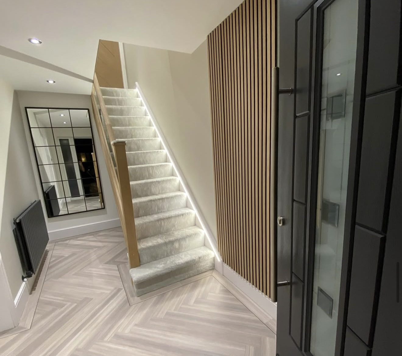 Pale grey herringbone hallway with a border around the foot of the carpeted stairs